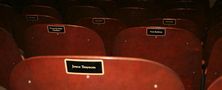 A view of the backs of theatre seats with engraves name plaques.