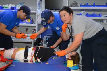 Three Chipola EMT students surround a patient on a backboard stretcher during a medical emergency simulation. 