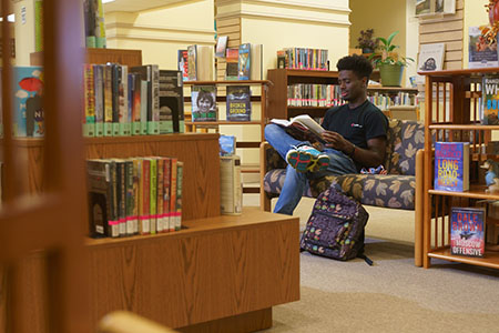 A student sits on a couch reading, surrounding by shelves of books in the Chipola Library.