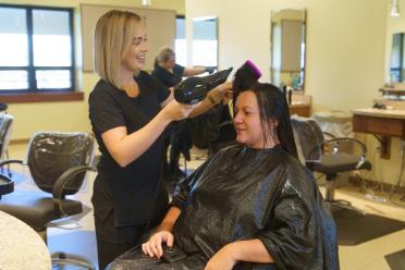 A Chipola College Cosmetology student uses a brush and hand dryer to dry a client's hair.