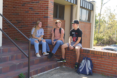 Three Chipola student sit talking on building steps and the adjoining wall.