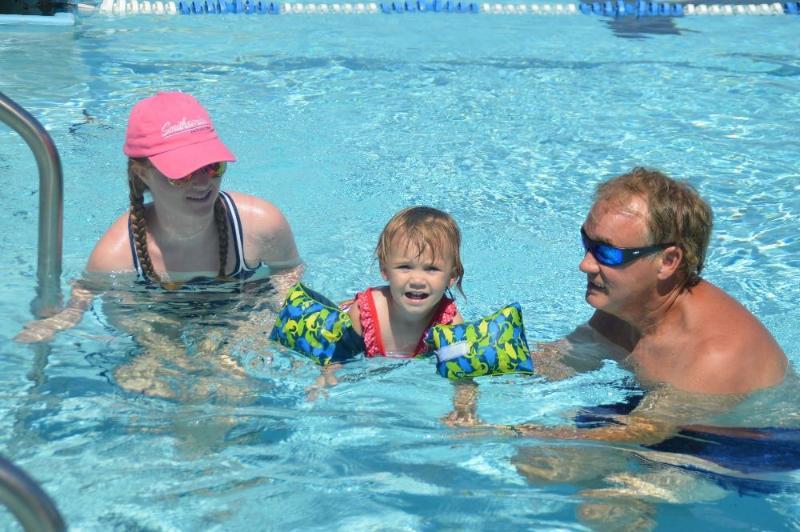 A woman, a child wearing floaties, and a man wade in a pool.