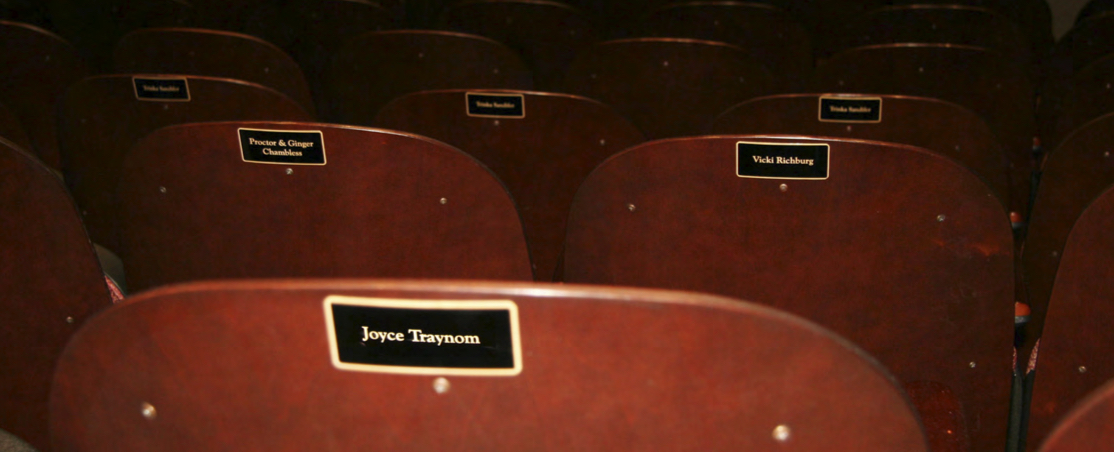 A view of the backs of theatre seats with engraves name plaques.