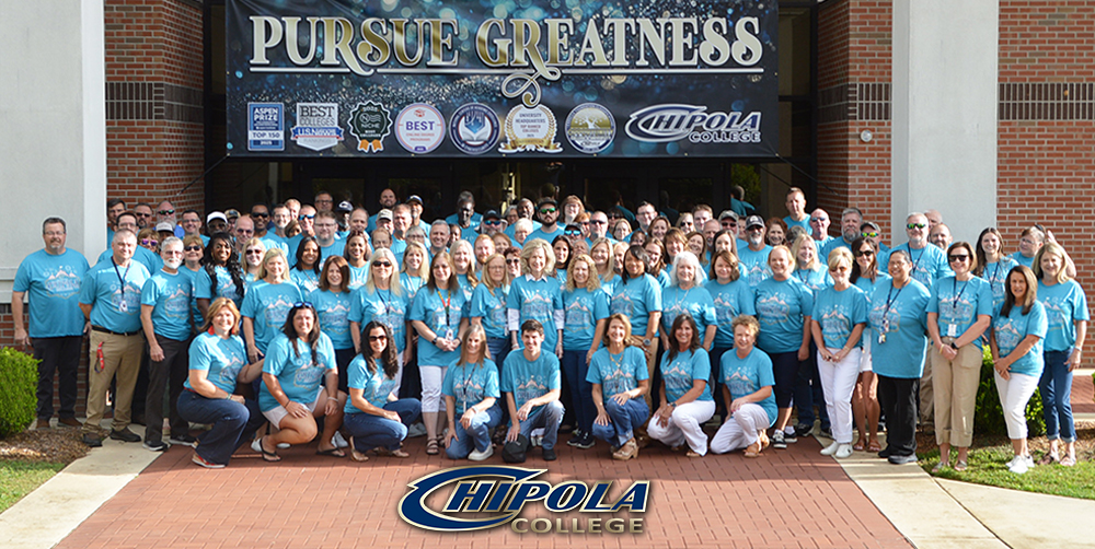 faculty and staff standing together outside posing in front of banner