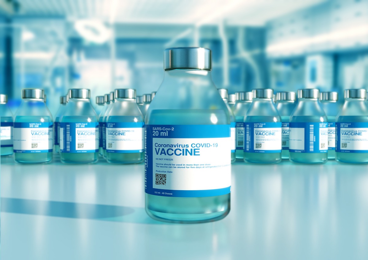 A bottle of COVID-19 vaccine sits in the foreground with rows of vaccine in the background.
